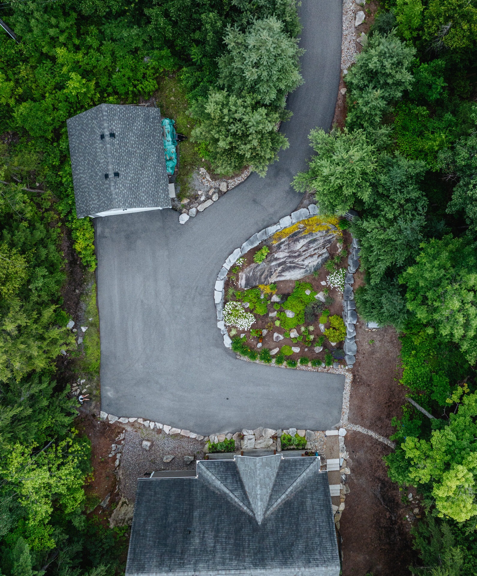 Aerial view of a house surrounded by lush trees, curved driveway, and landscaped garden, showcasing a serene, natural setting.