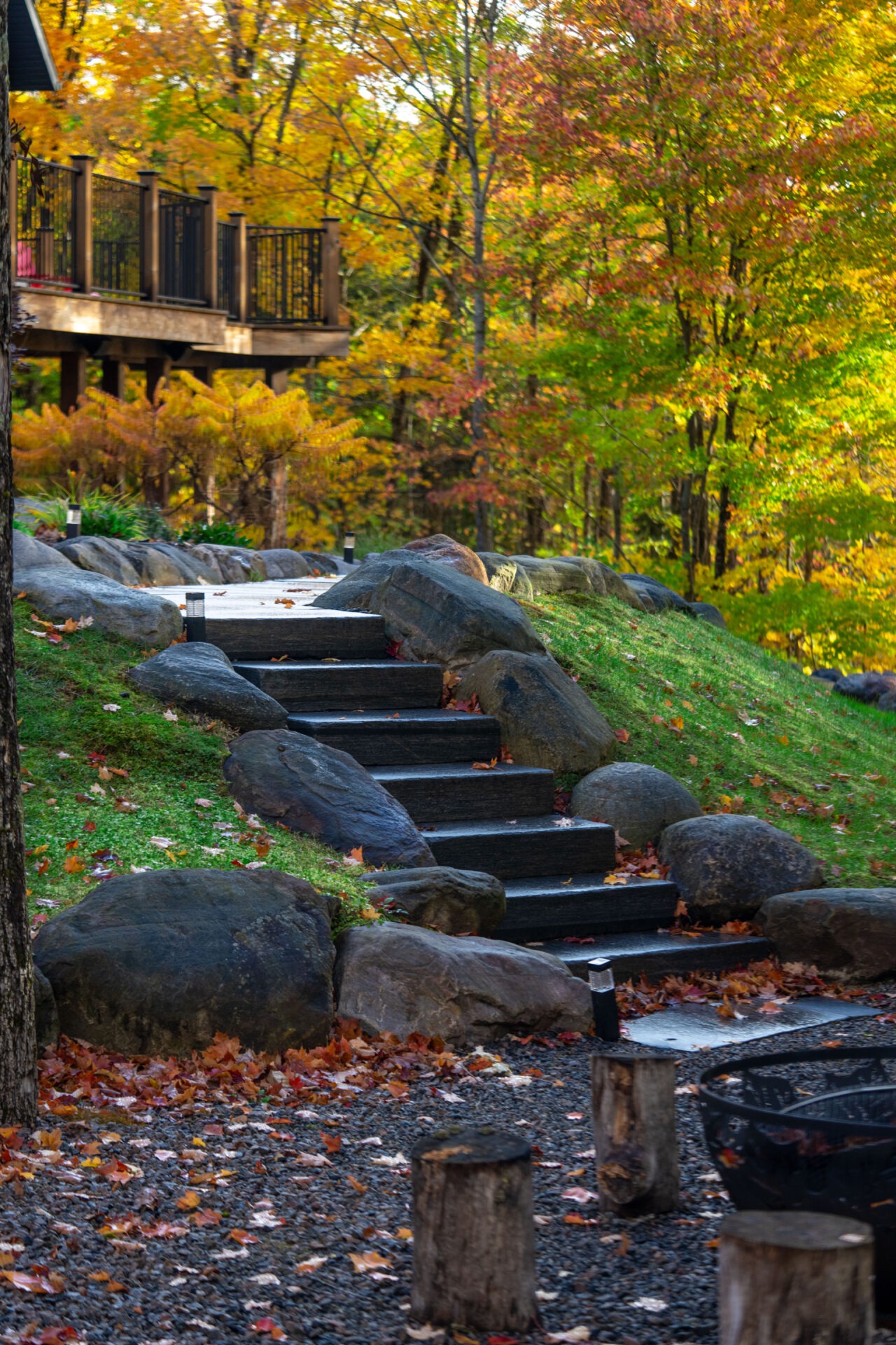 Stone steps wind through an autumn forest with colorful leaves, leading up to a wooden deck surrounded by vibrant trees.