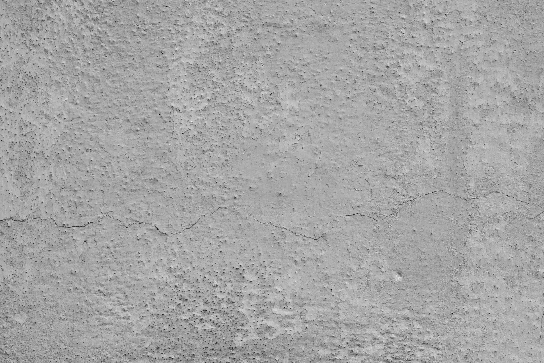 A close-up of a textured, cracked concrete surface showing signs of wear, with various indentations and rough patches visible across the surface.