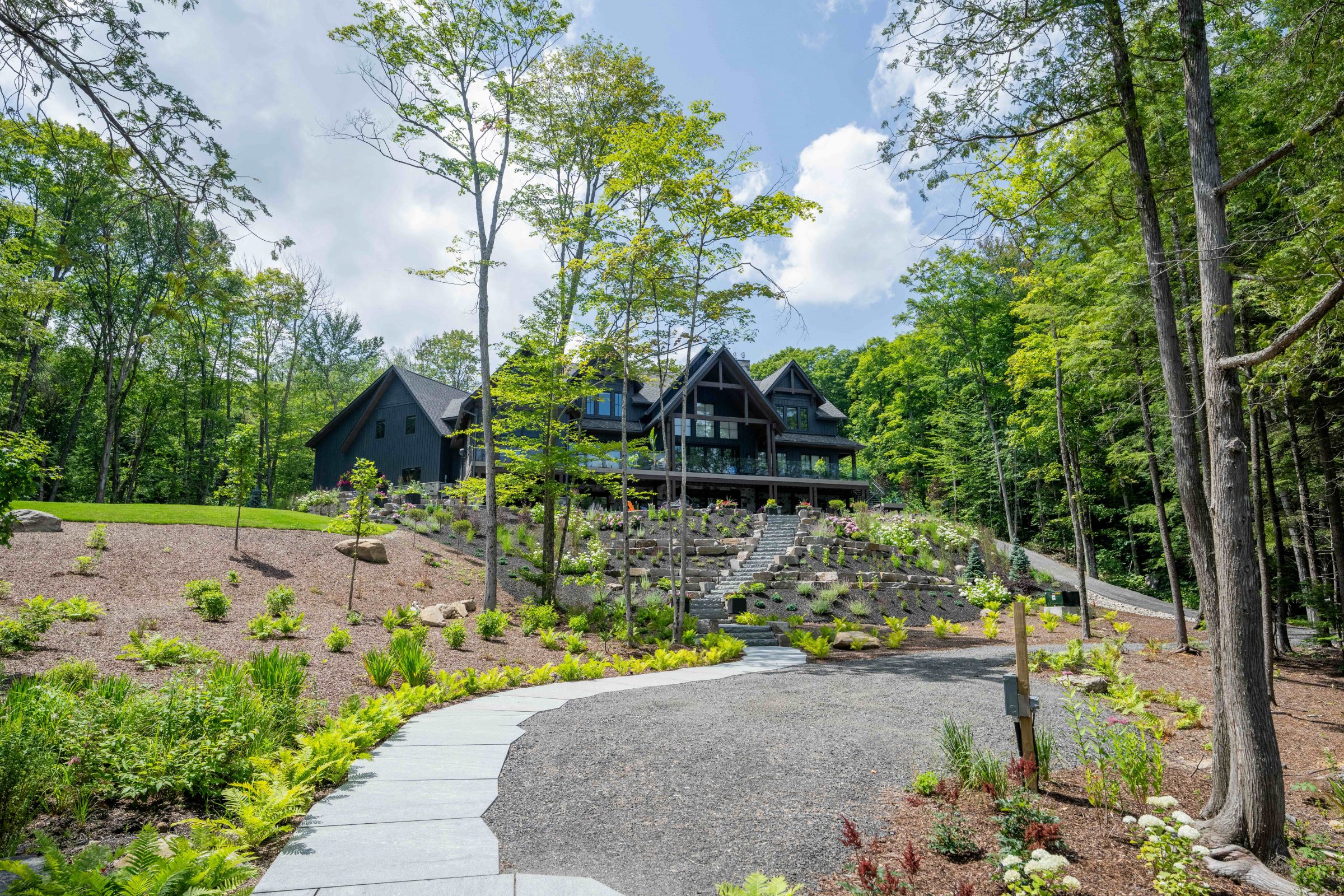 Custom-cut sawn granite walkway curving through a terraced, landscaped hillside toward a modern luxury Muskoka cottage.