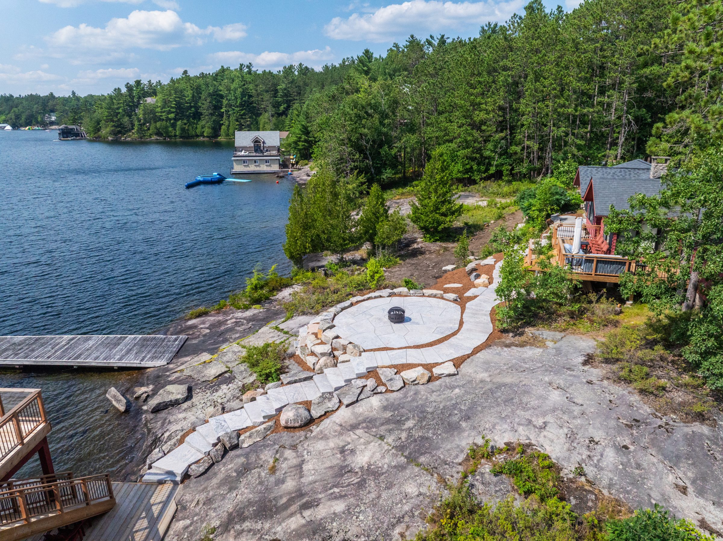 High-end Muskoka landscape design featuring a precision-cut circular stone patio, sawn steps, and a waterfront dock nestled in natural Canadian Shield bedrock.