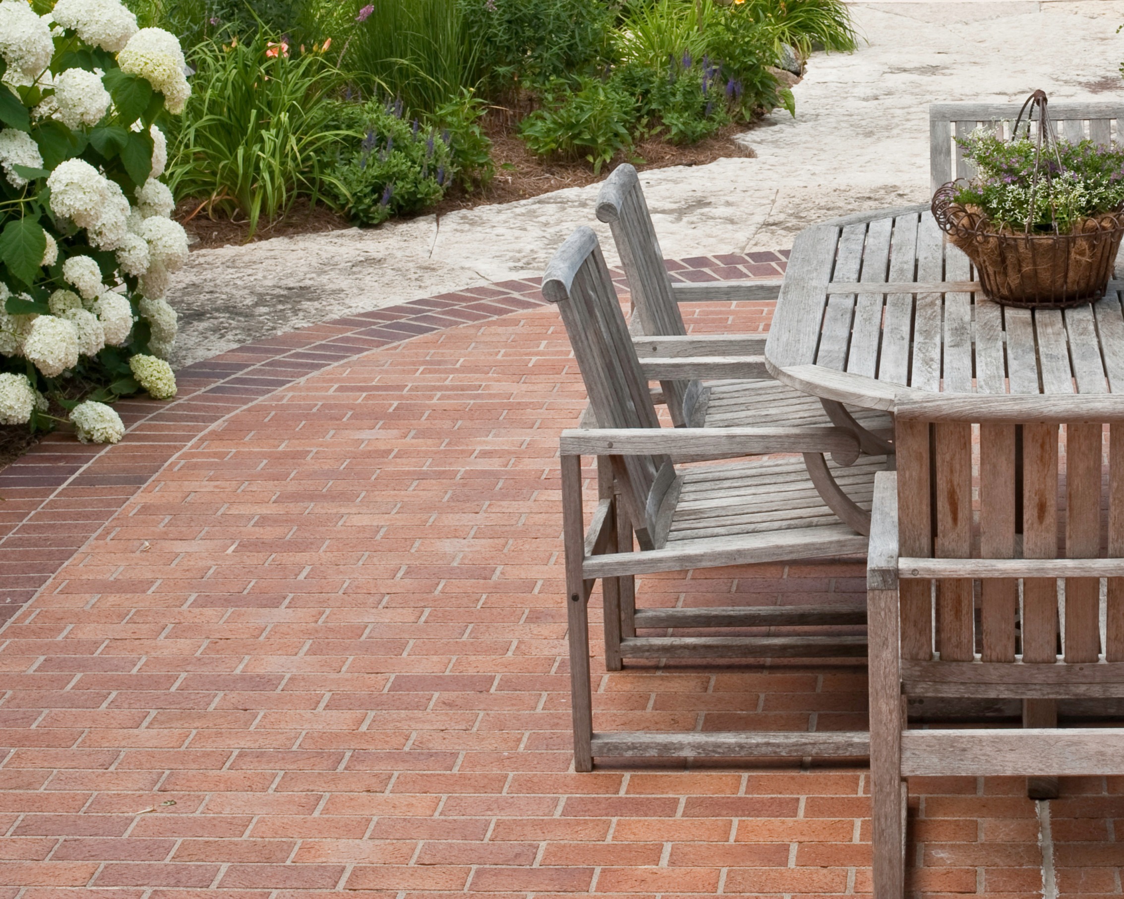 Red brick interlocking paver patio with wooden outdoor dining furniture and natural stone border.