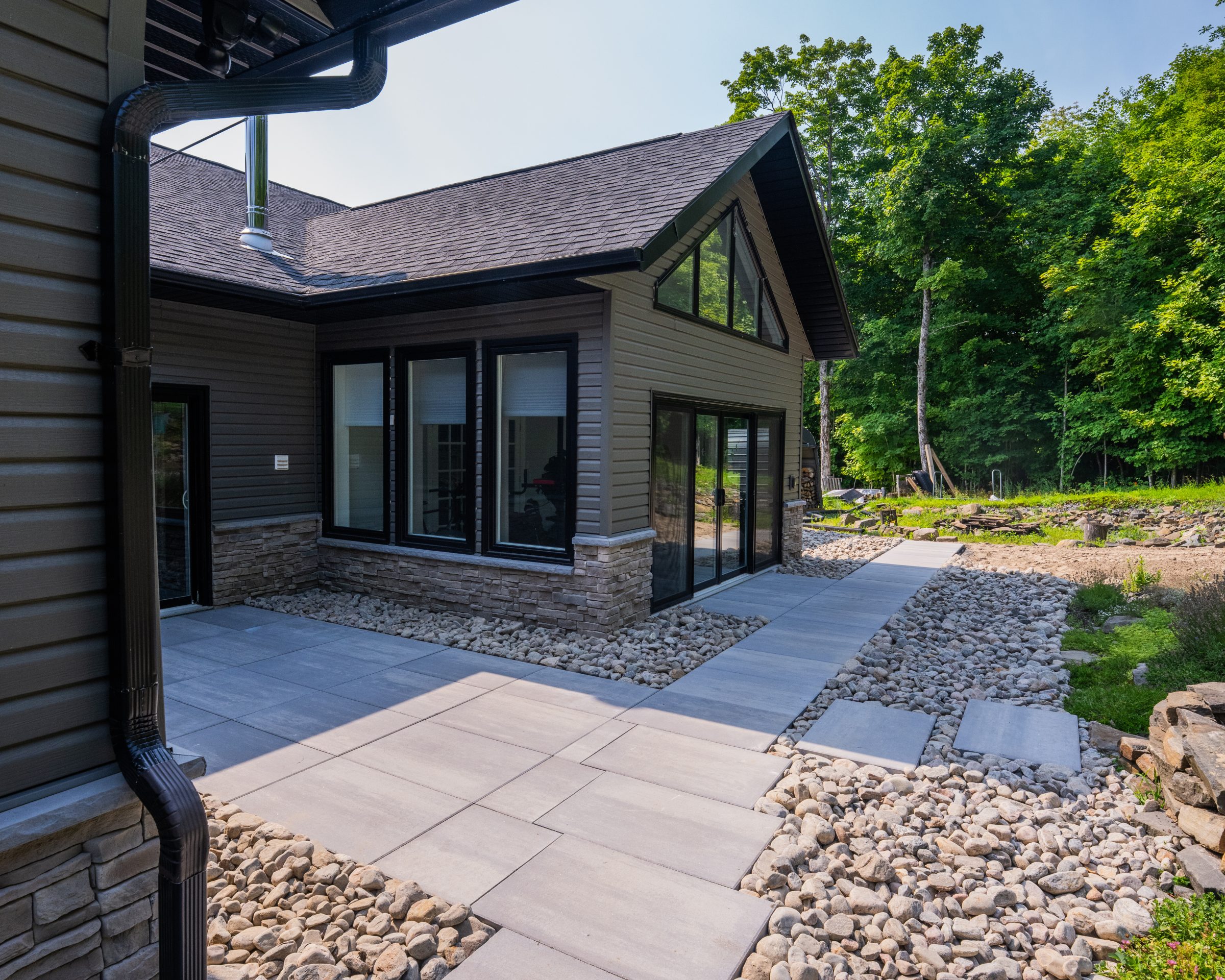 Large-format smooth concrete patio stones and walkway set within decorative river rock around a modern cottage.