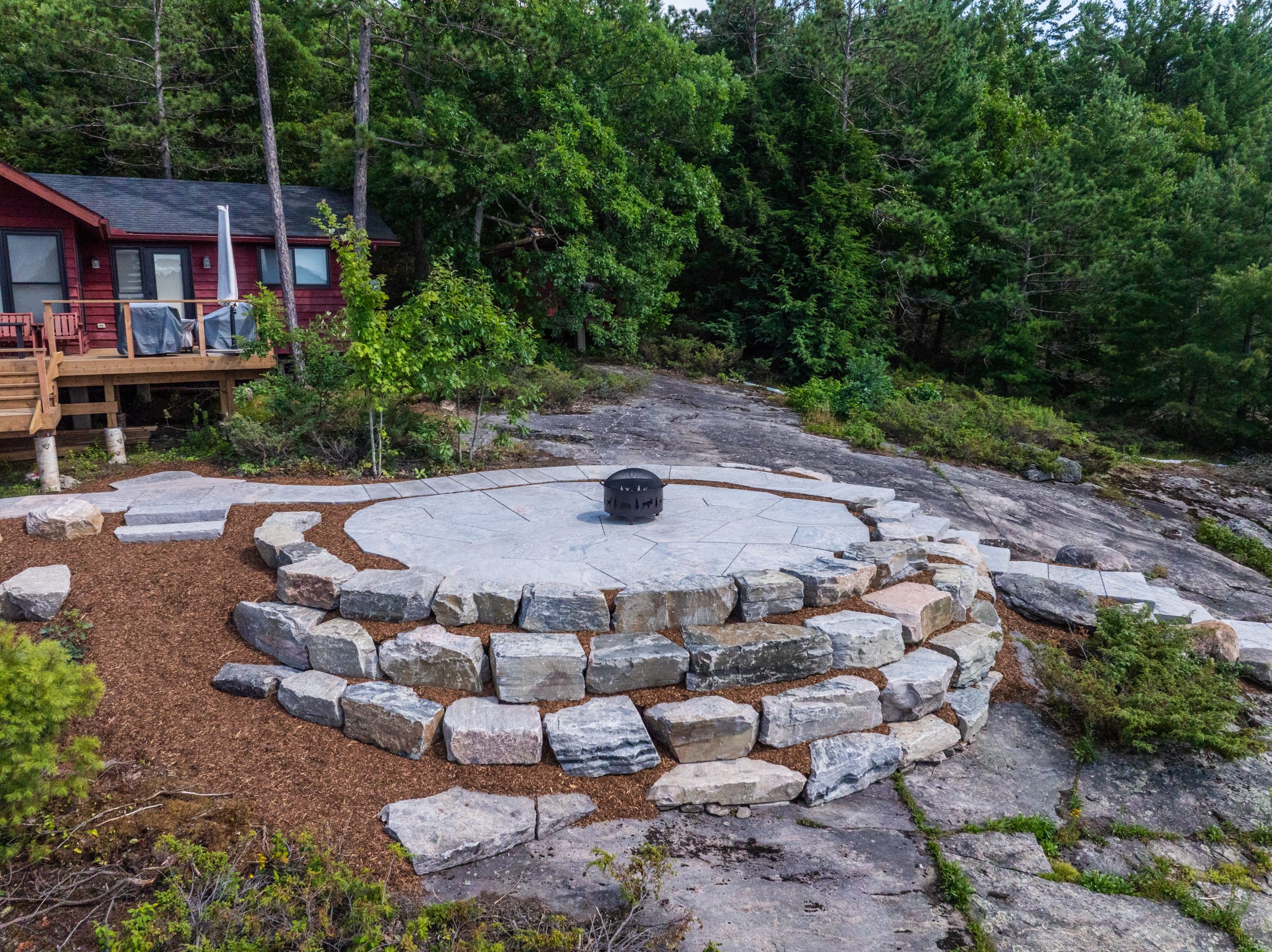 Custom stone patio integration featuring armour stone retaining walls and fire pit seating area.