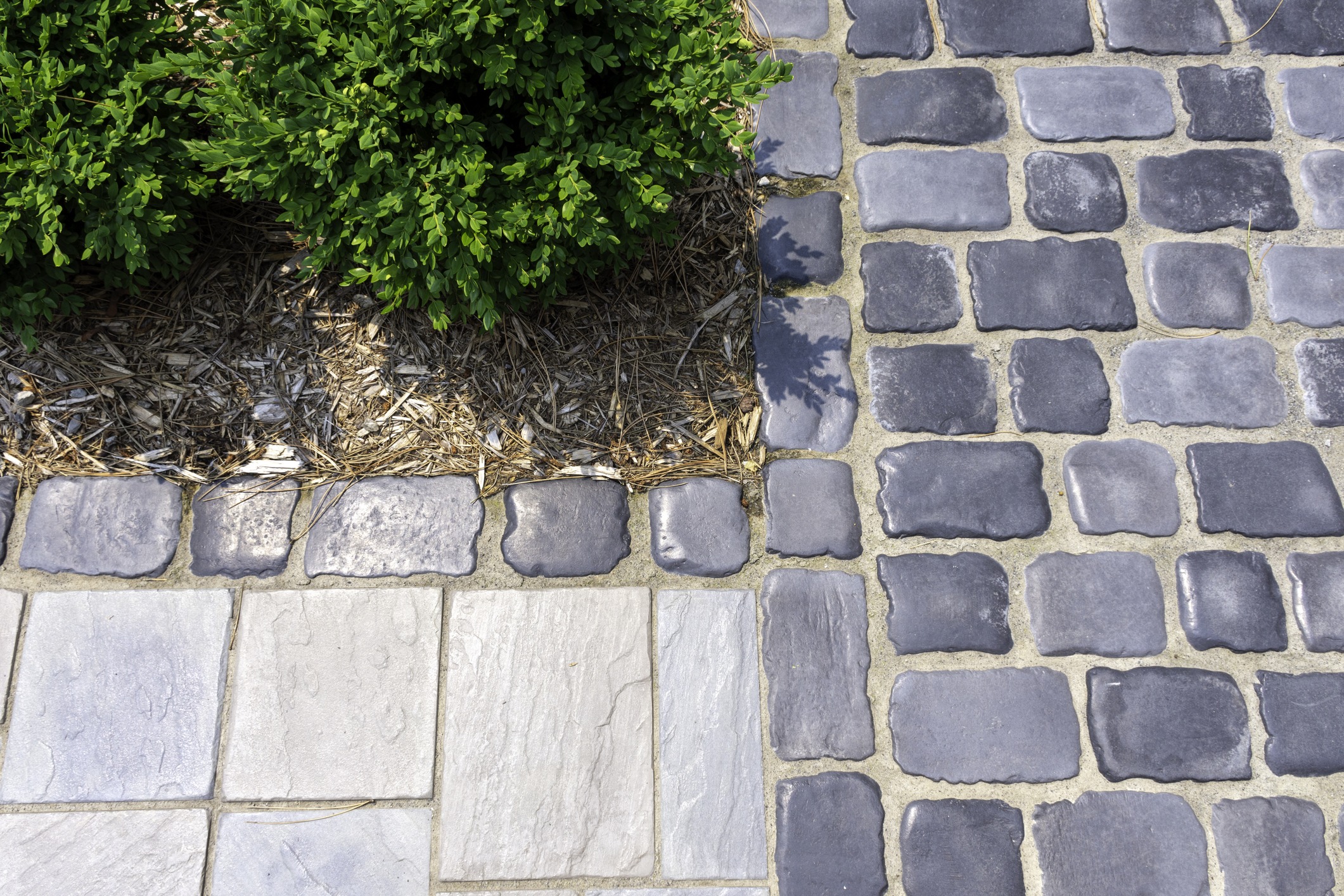 Close-up of cobblestone paver border and interlocking walkway next to a garden bed.